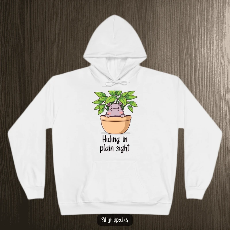Funny Hoodie illustration of a playful hippo peeking out from behind a big, leafy potted plant, looking curious.